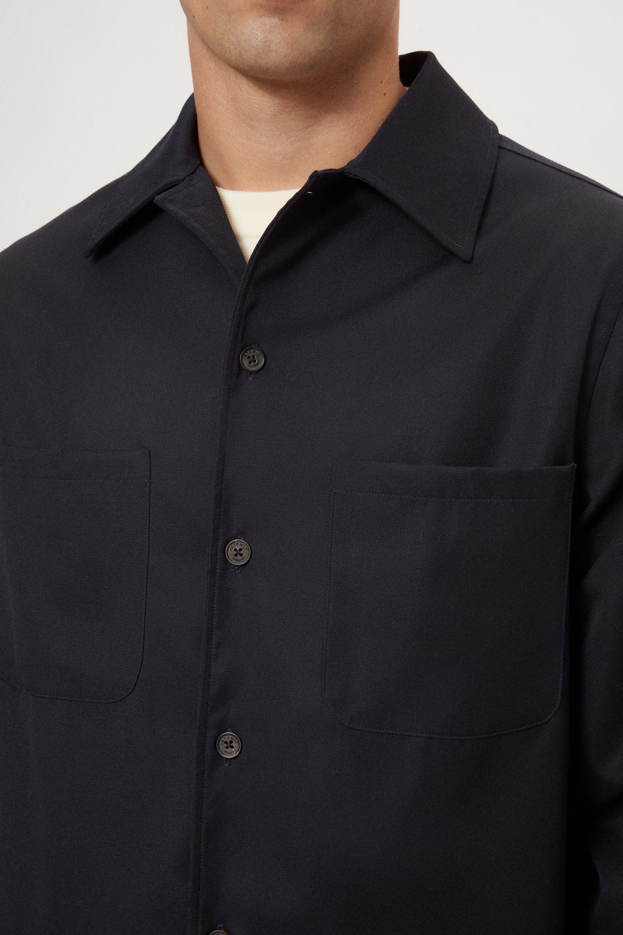 Man wearing a dark blue Twill Wool Overshirt over a white shirt on a light gray background