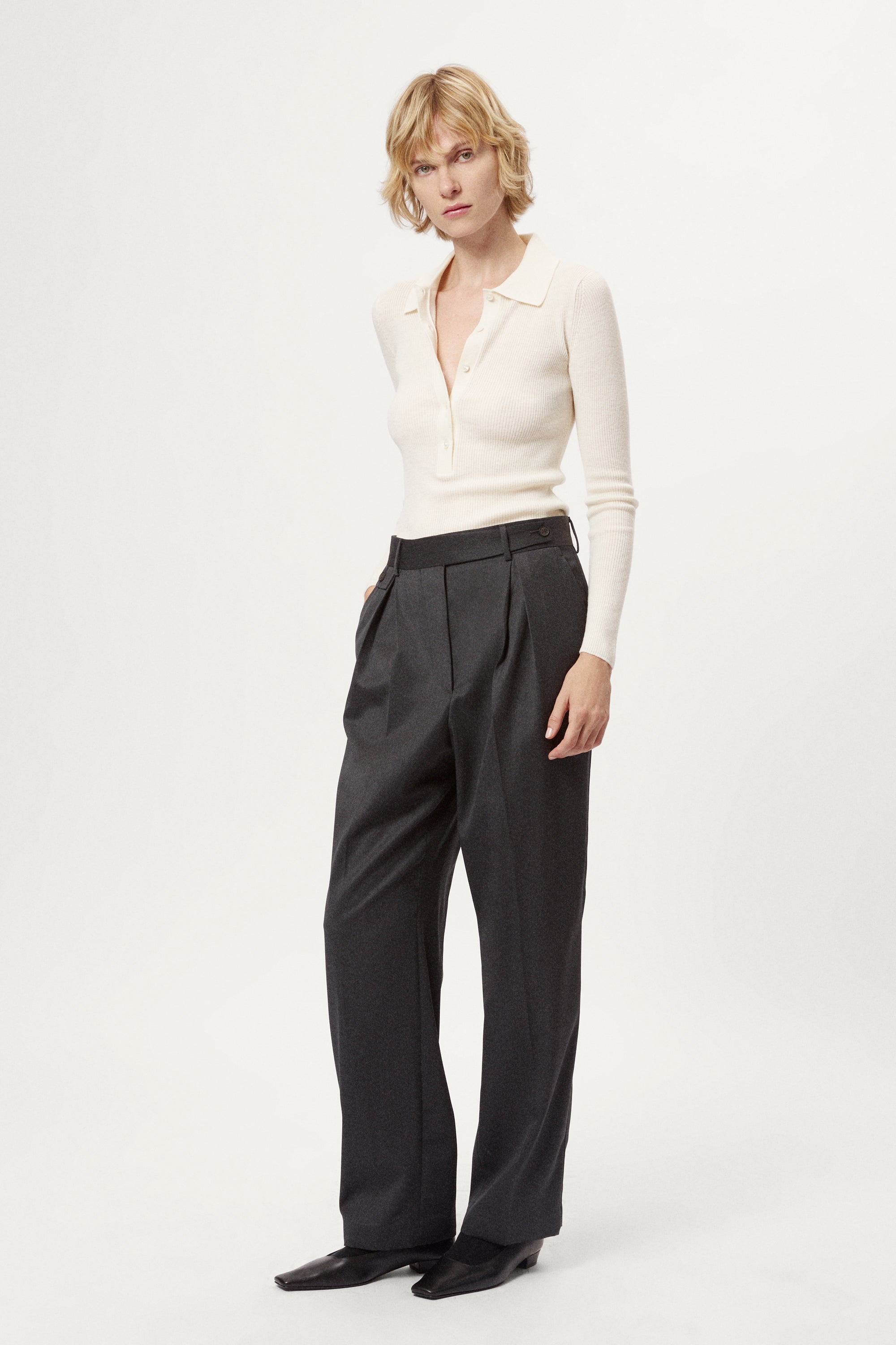 Woman wearing a white merino shirt and dark gray pants on a white background